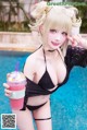 A woman in a black bikini holding a drink by a pool.