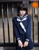 A woman in a school uniform standing in front of a gate.