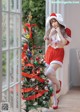 A woman in a santa outfit posing next to a Christmas tree.